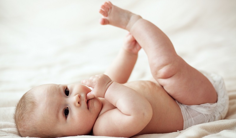 Eltern legen das Baby vor sich nackt auf den Boden und sehen ihm direkt ins Gesicht.  ( Foto: Shutterstock- Alena Ozerova )